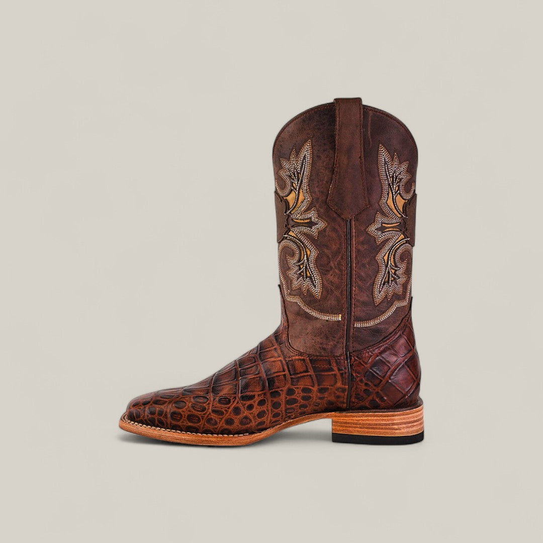 The Jonh - Brown - Square Toe boot features a crocodile-patterned lower section, decorative stitching on the shaft, and a stacked wooden heel, highlighting quality craftsmanship against a plain beige background.