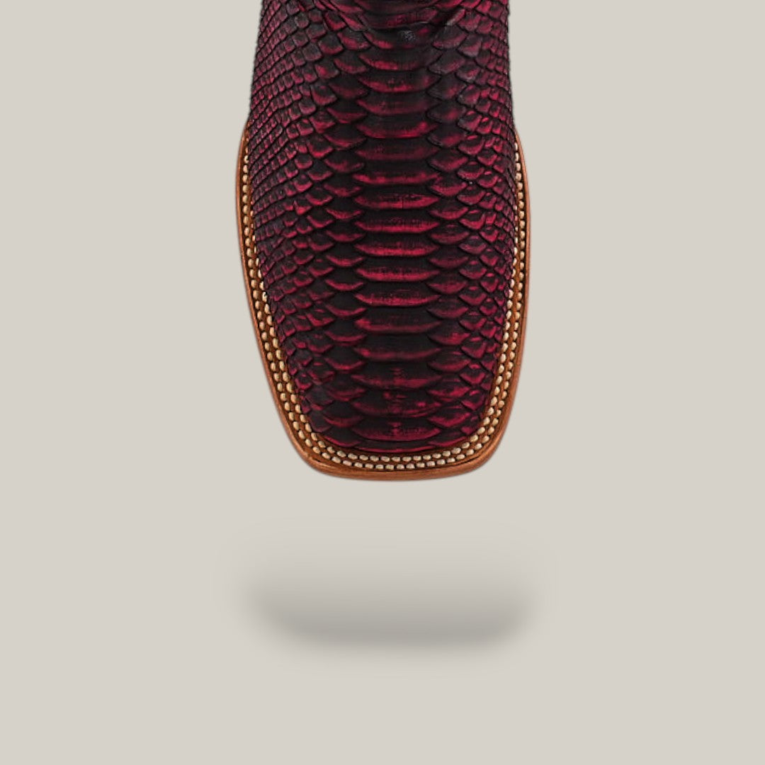 Close-up of the toe of the Exotic Python - Cherry Nobuck - Square Toe boot in a rich burgundy hue, featuring tan stitching around the sole, set against a plain light background.