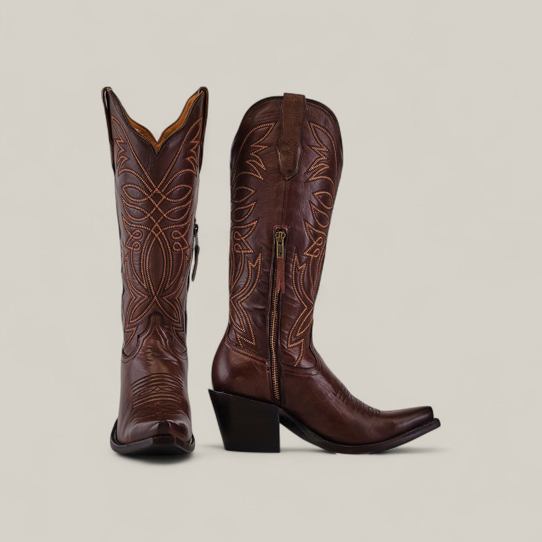 The Kellie Clayton Caramel Leather Sole boots feature a tall shaft, snip toe, angled heels, intricate stitching, decorative patterns, and zippers. One boot is shown facing forward and the other from the side.
