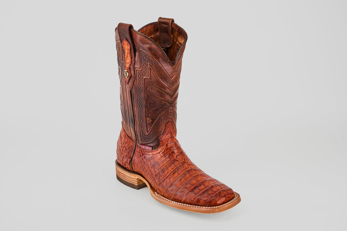 The Exotic Caiman Belly - Brandy - Square Toe boot features a rich brown hue, textured crocodile-like pattern, and decorative stitching, highlighting its luxurious exotic leather against a plain light gray background.