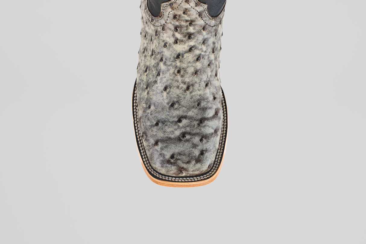 A close-up, top-down view of the Exotic Full Quilt Ostrich - Nicotine - Square Toe boot in textured gray ostrich leather with black speckles and a tan-and-black stitched sole, showcasing its expert craftsmanship.