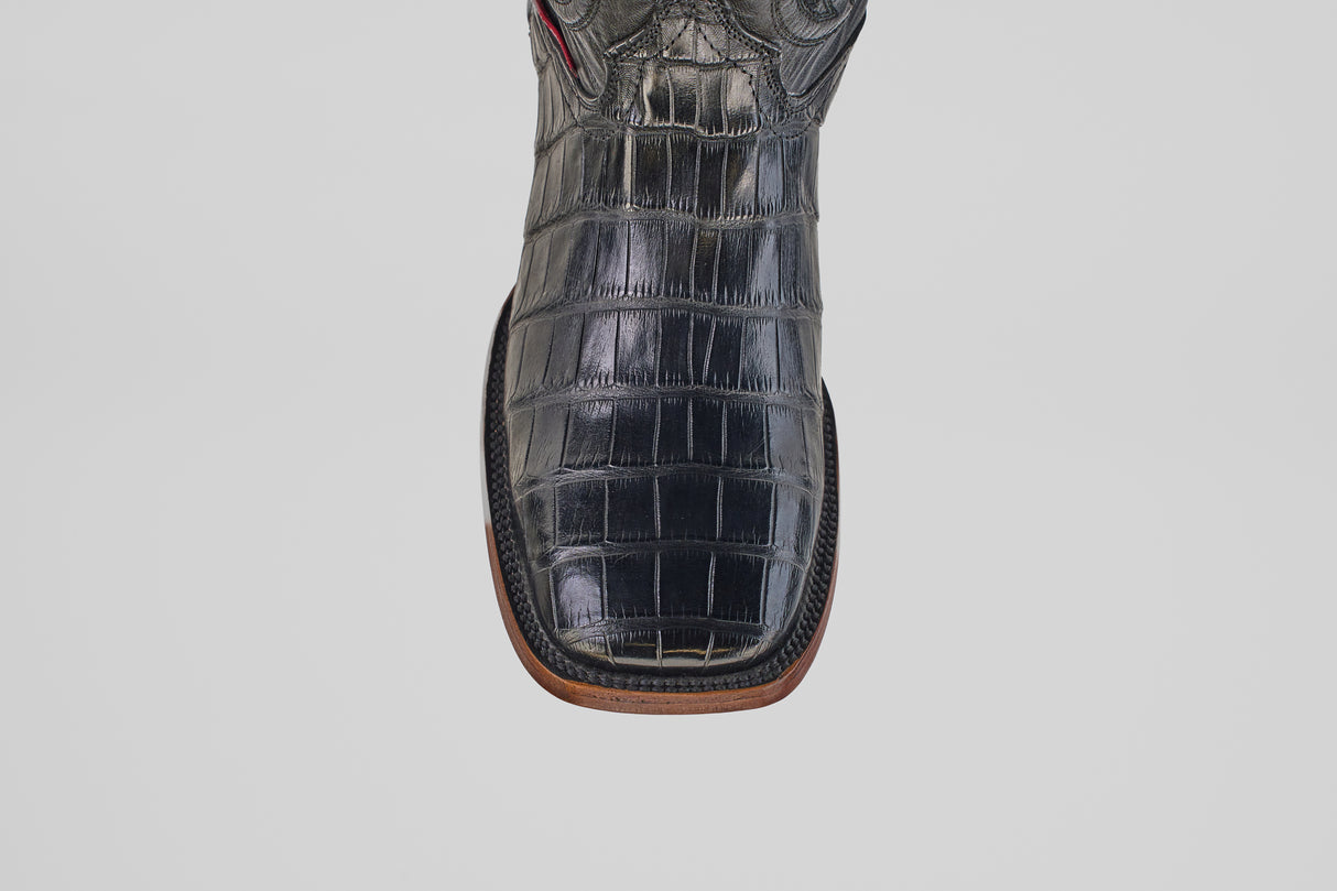 A close-up of the Exotic Alligator Tail - Black - Square Toe boot, featuring genuine alligator leather with a shiny finish, square toe, and brown sole, displayed against a plain light gray background.
