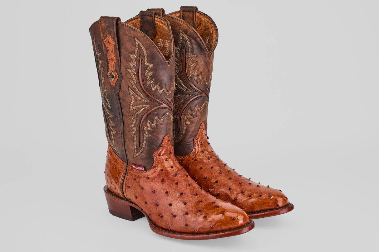 The Exotic Full Quilt Ostrich - Brandy - Round Toe boots feature handcrafted, textured ostrich leather with decorative stitching on tall, darker brown shafts, displayed against a plain light gray background.