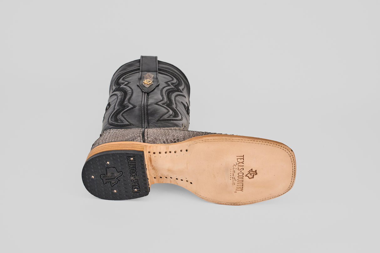 The Tanner - Matte Gray - Square Toe boots feature one upright and one on its side to display the Texas Country-branded sole, with a decorative stitched upper and textured Python Gris Nobuck lower section.