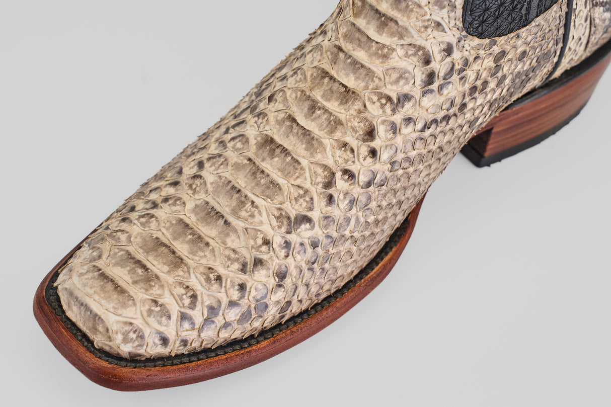 Close-up of the Tanner - Natural boots, crafted in beige python leather with a narrow square toe, showcasing detailed texture, a wooden sole, and black stitching.