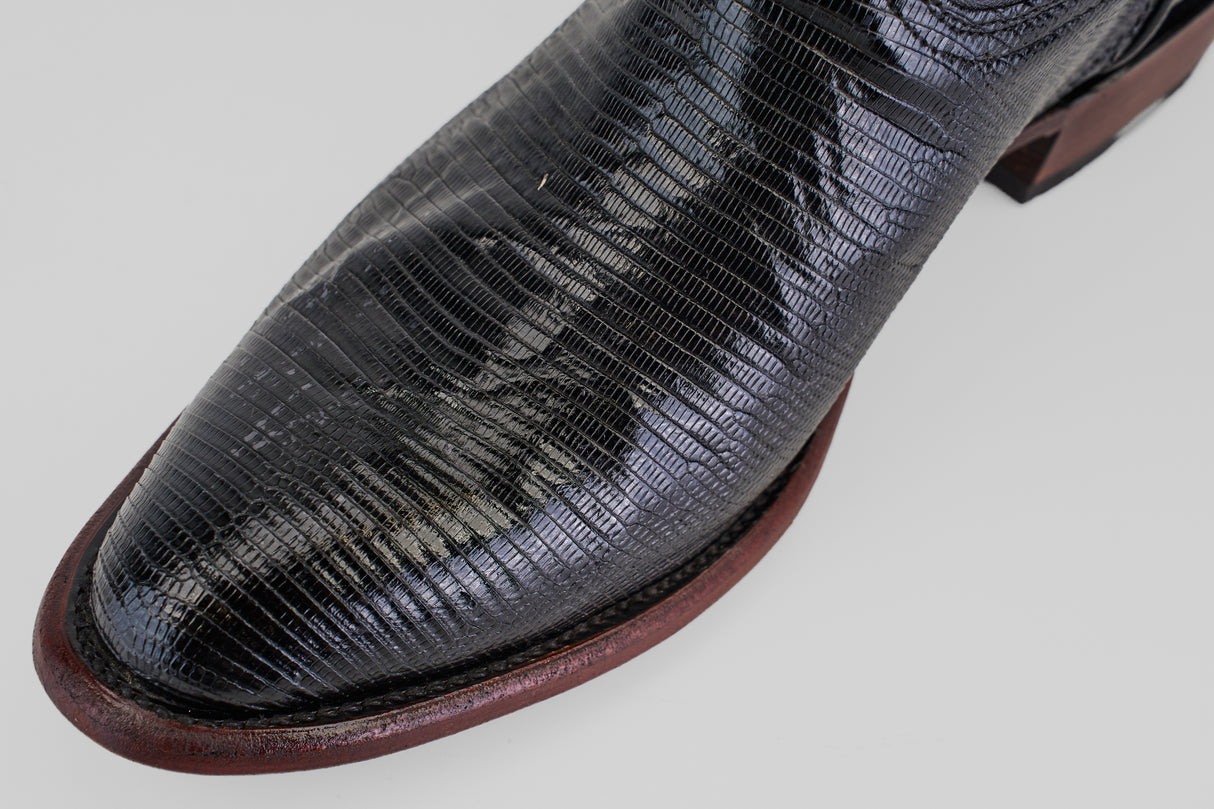 Close-up of the Blaze – Black – Round Toe shoe featuring shiny, textured black leather and a dark brown sole with detailed lines and a slightly worn look, set against a light background.