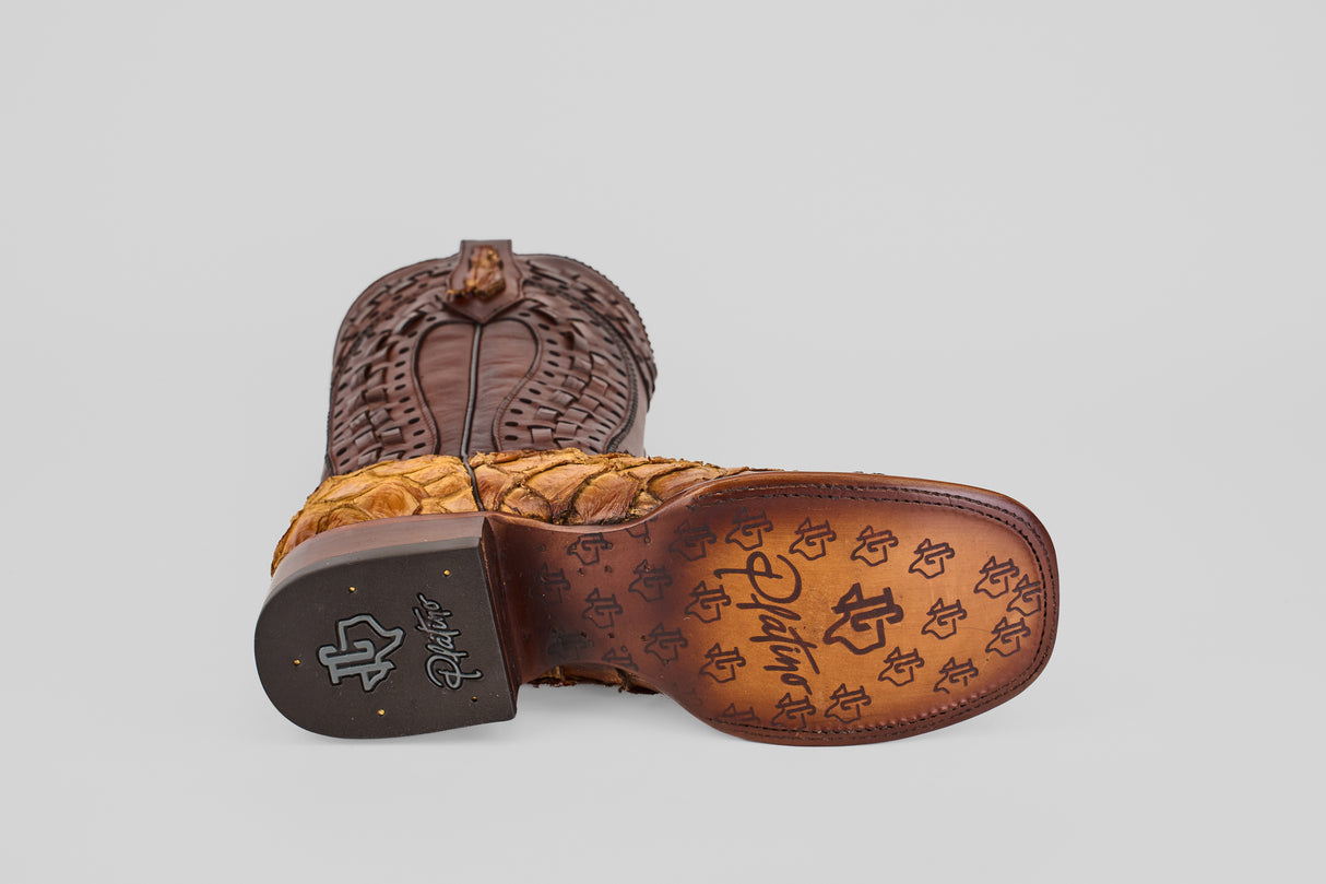 A single Conor Platinum - Buttercup - Square Toe (Herradura) cowboy boot lies on its side, displaying the “R” logo patterned sole, stitched detailing, and textured brown upper against a plain gray background.