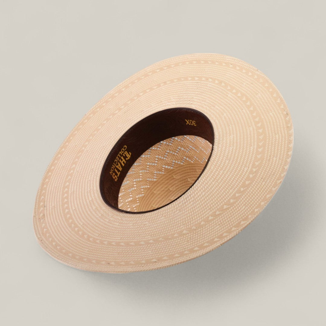 The 30X Zig Zag - Open Crown is a light-colored, wide-brimmed woven hat seen from above, highlighting its intricate patterns and a dark brown inner band with gold writing. Ideal for those seeking unique, timeless hat styles. Plain neutral background.