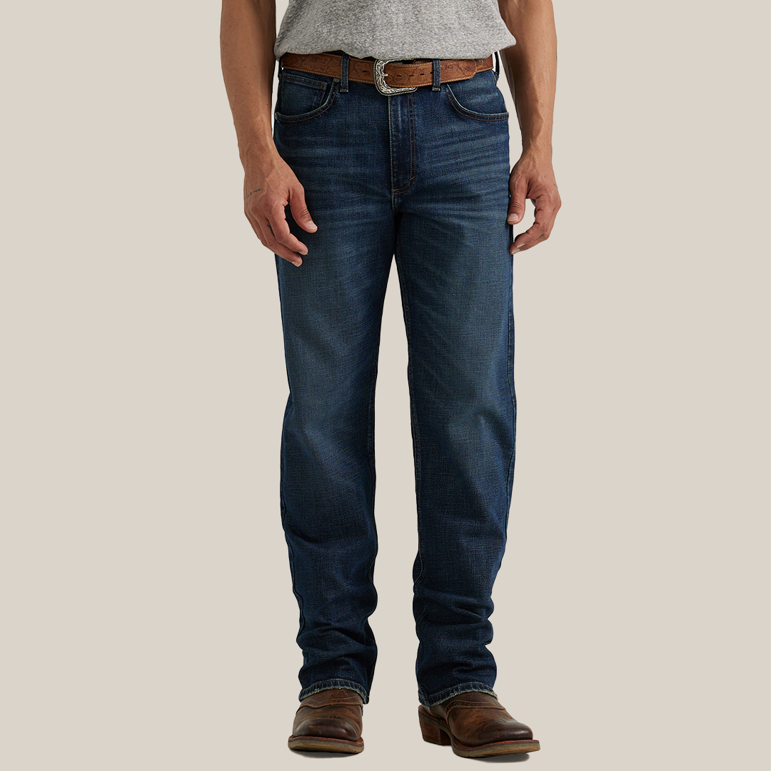 A person wearing a gray shirt, Wrangler 20X Sunnybrook Dark Wash Extreme Relaxed Straight Stretch Denim Jeans, a brown leather belt, and brown leather boots with a pointed toe stands against a plain background.