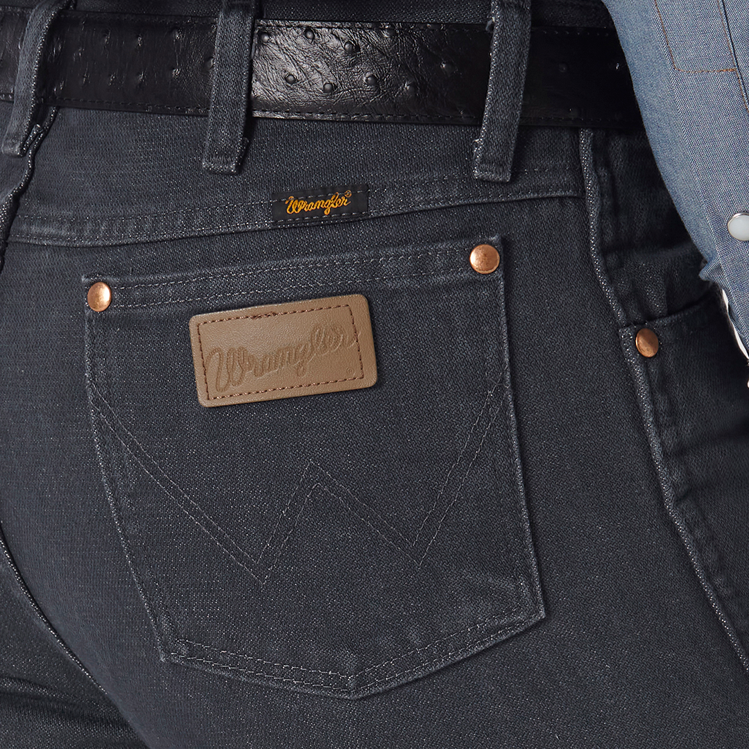 Close-up of a person in Wrangler Cowboy Cut Slim Fit Jean, 0936CHG, with visible pocket stitching and a brown leather label. Paired with a black belt and light blue shirt.