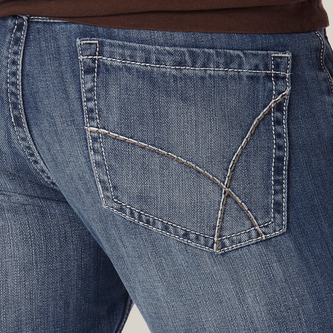 Close-up of a person in a plain, light-colored setting wearing brown shirt and Mens Wrangler 20X No. 42 Vintage Bootcut Jean - 1042MWXLB, featuring detailed back pocket stitching.