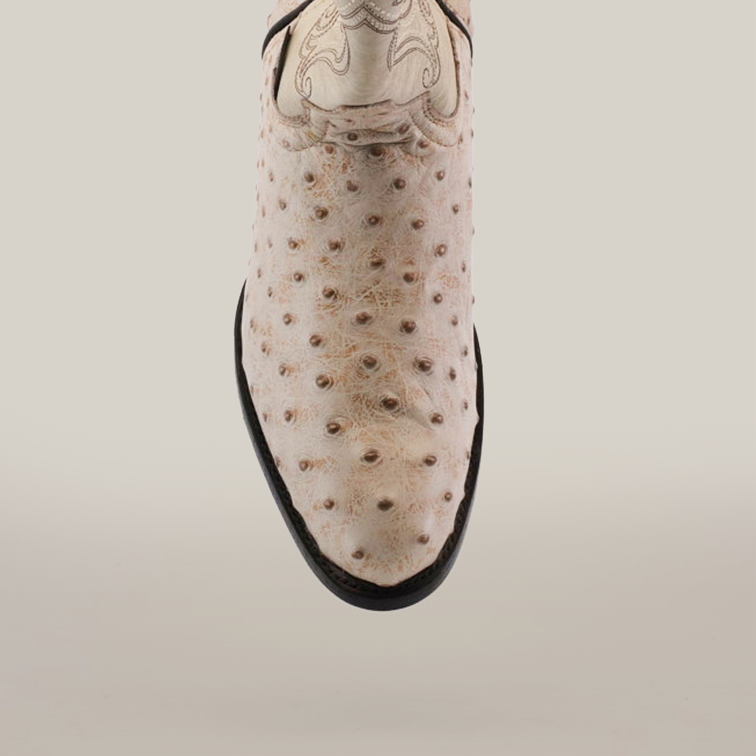 Close-up of the Karoo Ostrich Print Bone - Round Toe cowboy boot, featuring light-colored handcrafted ostrich leather with distinct textured bumps and elegant decorative stitching near the top, complemented by a smooth black leather sole.