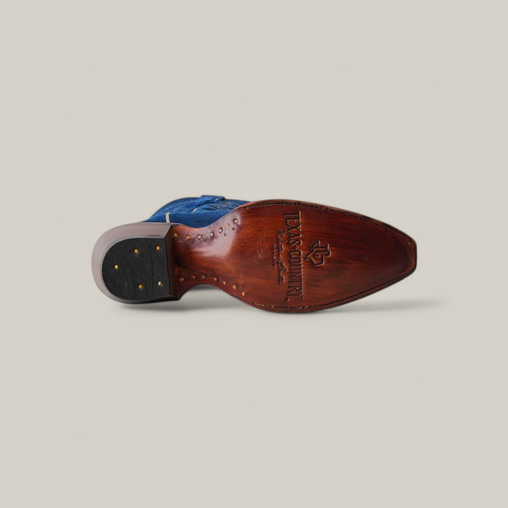 The image displays the sole of a Miranda Suede Blue Jeans Leather Boot with a snip toe design, featuring engraved Tecovas Handmade text. Gold nails are visible near the heel. The background is light gray.