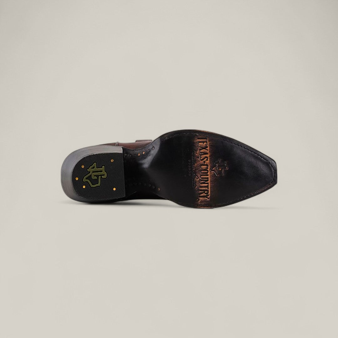 The Miranda Clayton Brownie Leather Sole boot features a TEXAS COUNTRY engraving and cross logo on the sole, plus a black and gold heel emblem—ideal for fans of classic, mid-shaft, snip-toe leather sole boots.