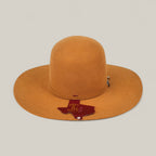 The 4X Caramel - TC Hats features a wide brim, camel color, open crown, decorative band, and a brown Texas-shaped tag on the brim, all displayed against a plain light background.