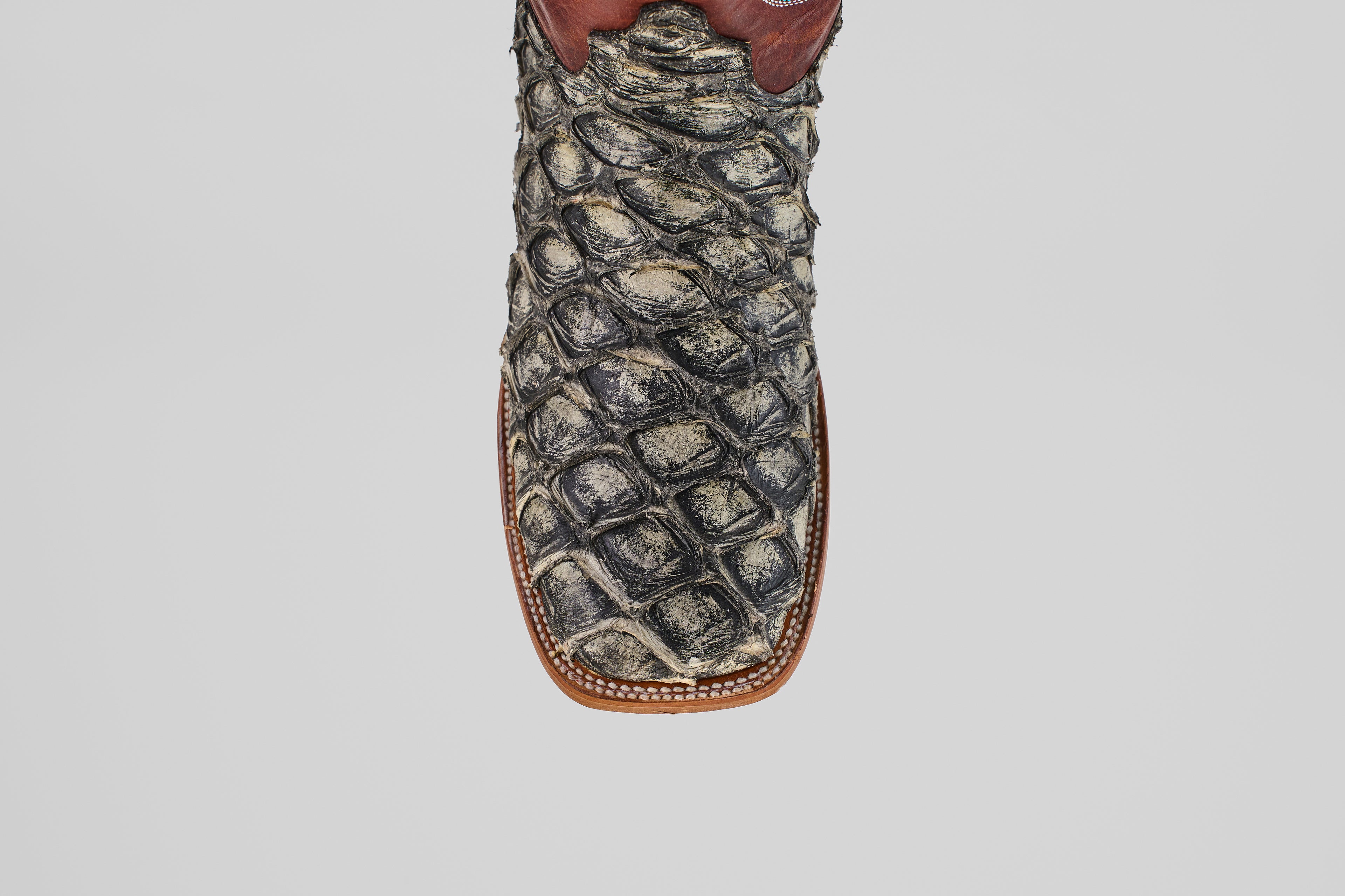 A detailed, top-down view of the Robinson - Newspaper - Square Toe boot highlights its textured Purarucu leather, brown trim, and white stitching—showcasing these distinctive handcrafted boots.