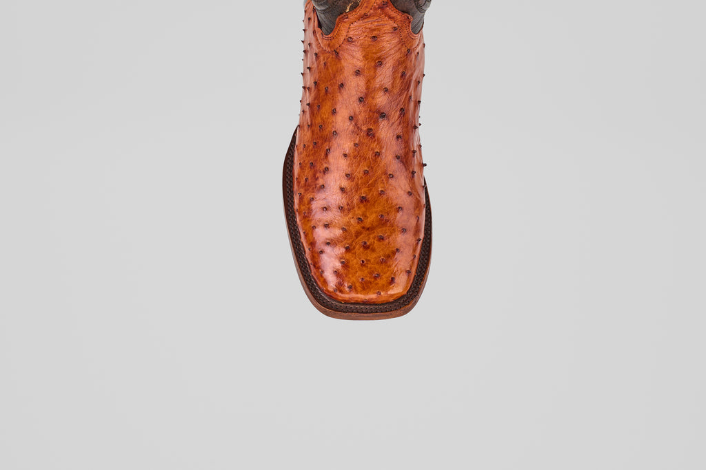 A detailed close-up of the toe of the Austin - Brandy - Square Toe cowboy boot shows its rich, bumpy brown leather texture and square tip, set against a plain light gray background.
