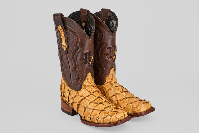 The Conor - Buttercup - Rodeo Toe boots feature fish leather with dark brown uppers, tan textured lower sections resembling scales, decorative stitching, and a slight heel, shown against a plain light background.