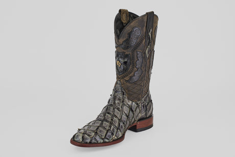 The Conor - Charcoal - Roper Toe is a men’s cowboy boot with scaly fish leather texture, decorative stitching, high shaft, brown and gray hues, roper toe, and a low wooden heel.