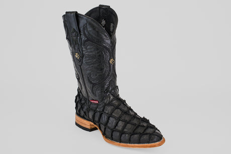 The Conor - Matte Black - Roper Toe boot features intricate stitching, a textured scale-like design inspired by pirarucu fish leather, and a light brown sole, shown on a plain gray background.