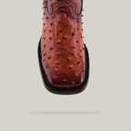 A close-up of the Exotic Karoo Ostrich - Platinum - Honey boot highlights its ostrich skin texture and distinctive square toe design, capturing the essence of classic cowboy culture against a plain backdrop.