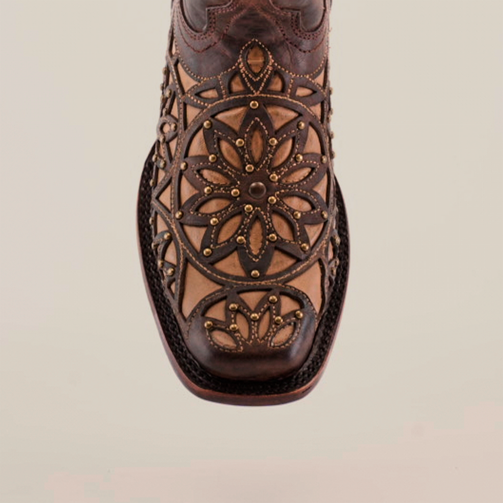 Close-up of handcrafted Vitralli Studs Tabaco boots highlighting intricate floral and geometric patterns on the toe, blending dark and light brown tones. Crafted from premium leather with decorative stitching, these mid-shaft boots feature a narrow square-shaped toe design.